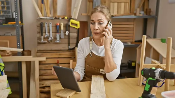 Concerned Woman Multitasks Her Workshop Talking Phone While Examining Tablet — Stock Photo, Image