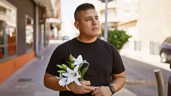 Hip, young latin man seriously brandishing a bouquet of flowers on a sunny city street, fashionably casual with a relaxed lifestyle