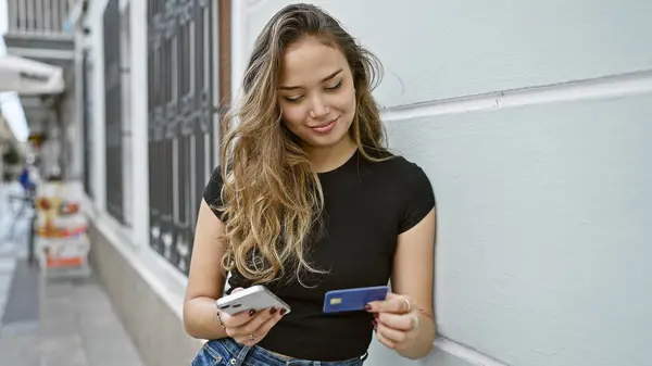 若い美しいヒスパニック系女性が通りのスマートフォンとクレジットカードで買い物 — ストック写真