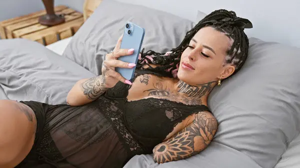 Confident hispanic amputee woman texting on smartphone, looking sexy in morning light, lying in bedroom