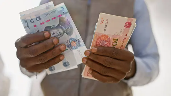 African man in formal wear holding chinese yuan and foreign currency on an urban street.