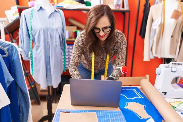 Young beautiful hispanic woman tailor smiling confident using laptop at atelier