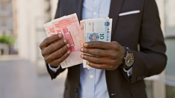 African man in suit holding chinese yuan and other currency on city street