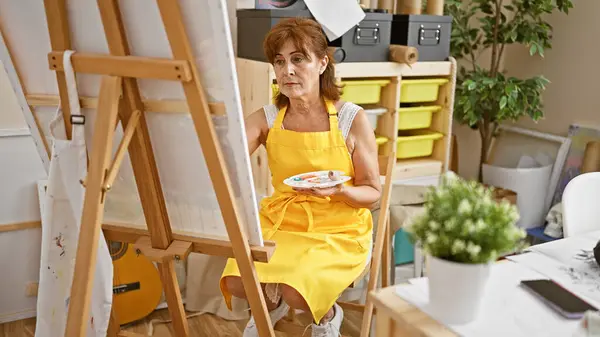 穿着黄色围裙的艺术工作室里的成熟女性绘画 提供了一个富有创意的教育理念 — 图库照片