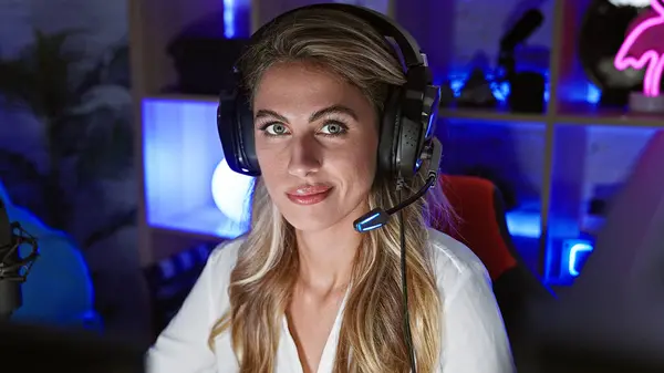 Fierce face off, young, attractive blonde streamer seriously engrossed in virtual gaming world, sitting solo in dark gaming room