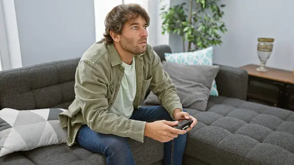 一个英俊的高加索人躺在沙发上 在现代客厅里玩电子游戏 — 图库照片