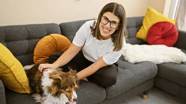 Hispanic woman smiling with glasses, petting her dog in a modern living room.