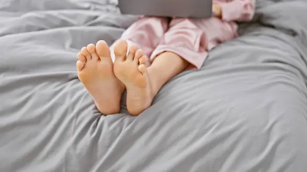一个穿着粉色睡衣的女人躺在床上 抱着笔记本电脑 躺在舒适的家庭环境中 放松下来 — 图库照片