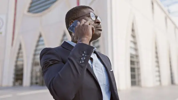 A professional african man in a suit uses a smartphone on a sunny city street.