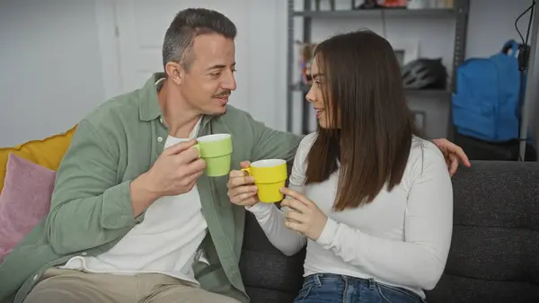 stock image A smiling couple enjoys a cozy moment with coffee in their modern living room, evoking love and comfort.