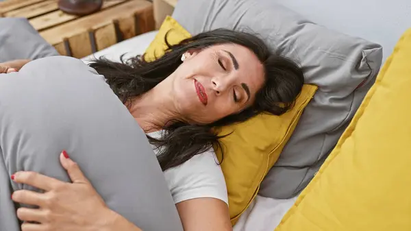 Middle-aged hispanic woman relaxing, eyes closed, in a cozy bedroom