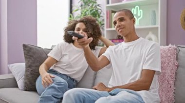 Güzel bir çift gülümsüyor, evdeki kanepede oturuyor, televizyon kumandası için şakacı bir kavgaya tutuşuyorlar..