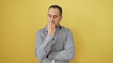 Gömlek giyen genç İspanyol adam gergin ve gergin görünüyor. Ağzı tırnak ısıran elleri var. Anksiyete izole edilmiş sarı arkaplan