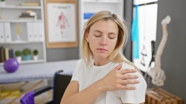 Kederli genç sarışın bir kadın, parlak bir rehabilitasyon kliniğinde omuz yaralanmasını inceliyor..