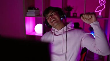 Young hispanic man streamer playing video game dancing at gaming room