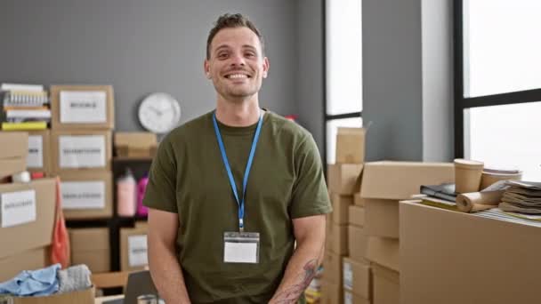 箱やオフィス用品に囲まれた倉庫に紙袋を持っているひげを持つ笑顔の若者 — ストック動画