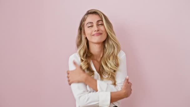 快乐的金发女子站在粉色的背景上 自信地拥抱自己 穿着衬衫 带着积极的快乐微笑 完全孤独 — 图库视频影像