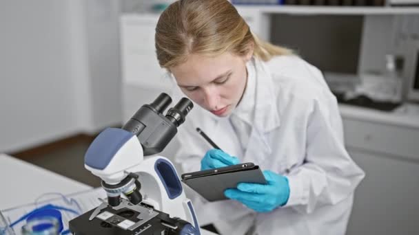 聚焦的女科学家在显微镜下研究样品 同时在实验室里做笔记 — 图库视频影像