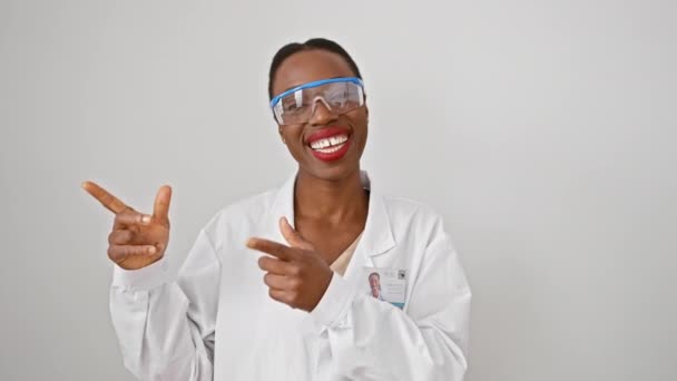身穿制服的快乐的非洲裔美国女科学家指向一边 自信地展示 微笑着 并在白色孤立的背景下看着相机 — 图库视频影像