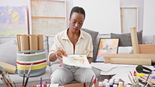 美しいアフリカ系アメリカ人女性アーティストがアートスタジオでノートブックを描くことに没頭 — ストック動画