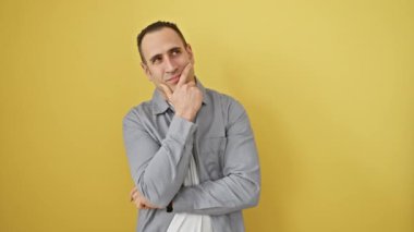 Tişörtlü, eli çenesinde bir soruyla güreşen dalgın, genç bir İspanyol. Yüzünde düşünceli bir ifade, sarı izole bir arka plana karşı sırıtıyor. Yüzüne kazınmış şüphe.