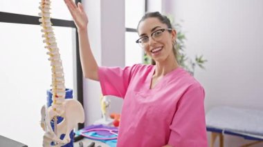 Işıldayan genç İspanyol kadın fizyoterapist, rehabilitasyon kliniğinde omurilik sağlığını anatomik modelle açıklıyor.