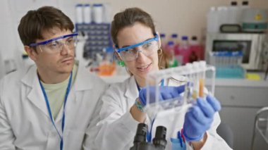 Erkek ve kadın bilim adamları laboratuarda test tüplerini birlikte inceliyor.