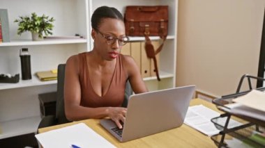 Afrika kökenli Amerikalı iş kadını gözlüğünü çıkarıp ofisteki dizüstü bilgisayardaki iş sorunları için endişeleniyor..