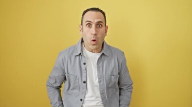 İspanyol adam, afallamış ve korkmuş, inanılmaz bir şok! Tamamen şaşırmış, korku dolu bir yüz ifadesi. Tişört giyiyor, sarı bir arka planda tek başına duruyor..