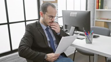 Sakallı ve gözlüklü konsantre olmuş kel adam ofis ortamında belgeleri inceliyor.