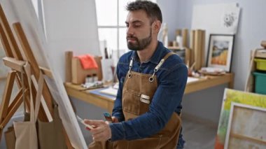 Genç, yakışıklı İspanyol ressam konsantre oluyor, önlüğe sarılmış, sakalı vurgulanıyor, stüdyo içi odaklanmış, resim akademisinde resim dersi alıyor, tuvalde fırça darbelerini öğreniyor..