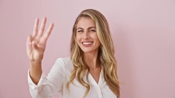 陽気な若いブロンドの女性はシャツを寄付し 自信を持って笑顔の表情で3本の指を指差し 孤立したピンクの背景の上に幸せなコンセプトのための番号3を伝えます — ストック動画