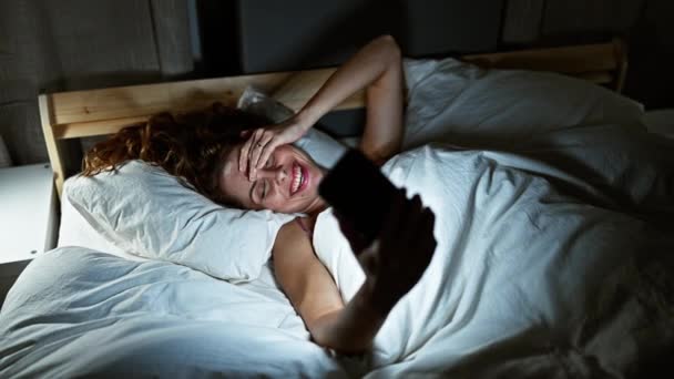 Улыбающаяся Молодая Женщина Лежит Постели Используя Смартфон Ночью Помещении — стоковое видео