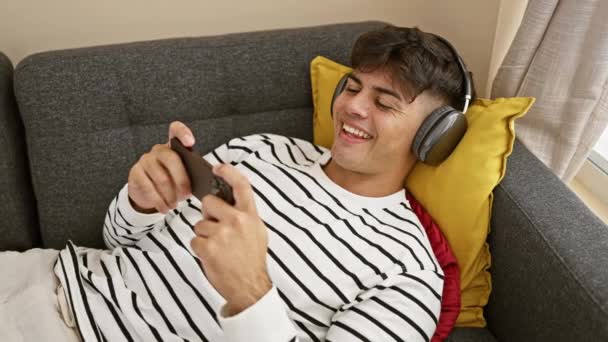 Jovem Homem Hispânico Confiante Ganhando Jogo Seu Gadget Enquanto Deitado — Vídeo de Stock
