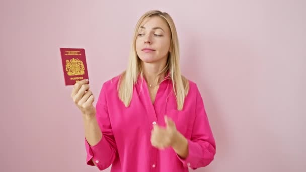 思慮深い若いブロンドの女性 混乱したアイデア 大胆に北アイルランドのパスポートを振る舞う 鮮やかなピンクの背景で孤立した中国の手 — ストック動画