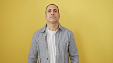 Kendinden emin ve pozitif düşünen, tişört giyen, kollarını kavuşturup çenesini kapatan, izole edilmiş sarı arka planda kameraya gururla gülümseyen genç İspanyol.