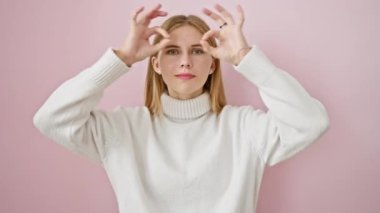 Eksantrik sarışın güzellik dilini dışarı çıkarıyor, arsız bir şekilde pembe arka plan üzerinden işaret parmaklarının arasından bakıyor.