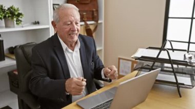 Neşeli bir kıdemli iş adamı, özgüvenli bir işçi, ofis masasında dizüstü bilgisayarla çalışırken başarıyı kutluyor.