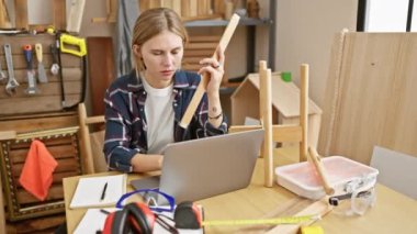 Odaklanmış bir kadın, marangozluk atölyesindeki ahşap parçayı aletler ve dizüstü bilgisayarla inceliyor..