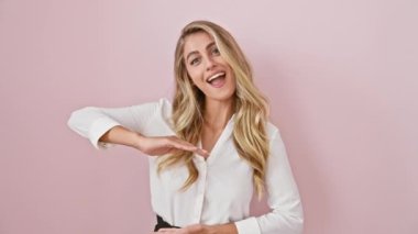 Pembe izole edilmiş arka planda duran neşeli sarışın kadın, tişört giyiyor ve elleri ile büyük boy bir sembol gösteriyor, gülümseyerek büyük bir ölçü kavramı işaret ediyor..