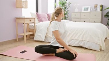 Genç sarışın kadın, parlak bir yatak odasında yoga yapıyor.