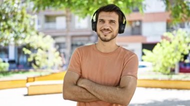 Canlı şehir parkında gülümseyen kulaklıklı kendine güvenen Latin adam.