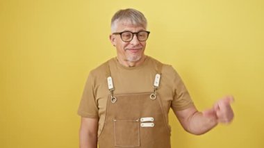 Gri saçlı, gözlüklü ve önlüklü, sarı arka planda duran, küçük beden işareti yapan orta yaşlı kendinden emin bir adam. bir ölçü konsepti verir.