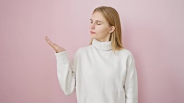 Neşeli, güzel, sarışın kız neşeyle sunar, avuç içini gösterir, izole edilmiş pembe arka planda durur, çekici bir reklam programına gönülden hoş geldin der.