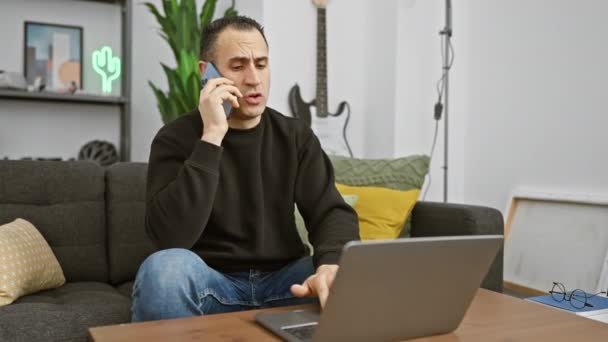 Geconcentreerde Spaanse Man Die Laptop Gebruikt Telefoneert Een Moderne Woonkamer — Stockvideo
