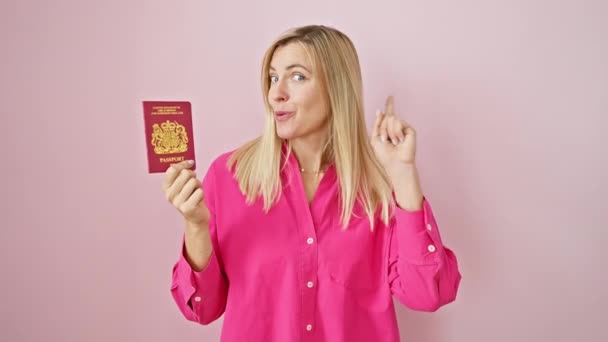 ハッピーな顔で北アイルランドのパスポートで若いブロンドのポイントを驚かせ アイデアで爆発し ピンクの孤立した背景の上にナンバーワン — ストック動画