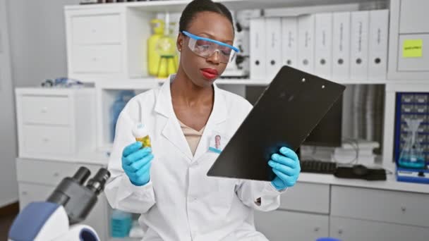 在认真的科学研究中 非洲裔美国女科学家正在一个专业实验室认真阅读有关药丸的文件 — 图库视频影像