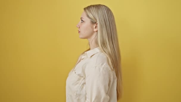 自信的金发女子摆出自然的姿势 站在旁边 笑容满面 在生机勃勃的黄色背景上隔离 — 图库视频影像