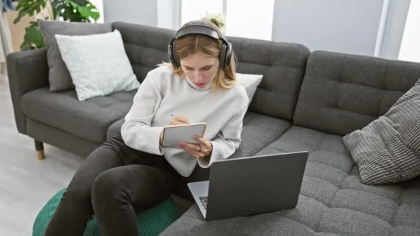 Sarışın Bir Kadın Evden Çalışıyor Kulaklığı Laptopu Olan Bir Puf — Stok video