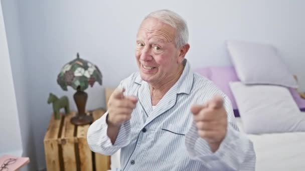 一个兴高采烈 精力充沛的老人 穿着可笑的睡衣坐在卧室的床上 高高兴兴地微笑着对着你指指点点 — 图库视频影像